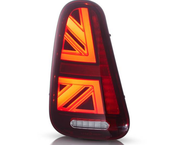 A red automotive tail light with illuminated chevron patterns is positioned upright against a plain white background. It features a horizontal white reflector at the bottom.