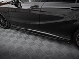A sleek black car is parked on a geometric-patterned, gray floor. The car has tinted windows and black alloy wheels, reflecting a striped ceiling above.