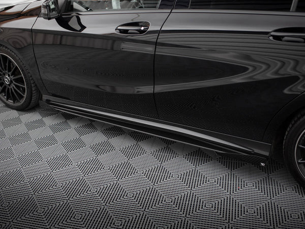 A sleek black car is parked on a geometric-patterned, gray floor. The car has tinted windows and black alloy wheels, reflecting a striped ceiling above.