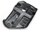 A carbon fiber automotive component with multiple molded sections and cutouts, including a central circular hole and various clips, lies on a white background.