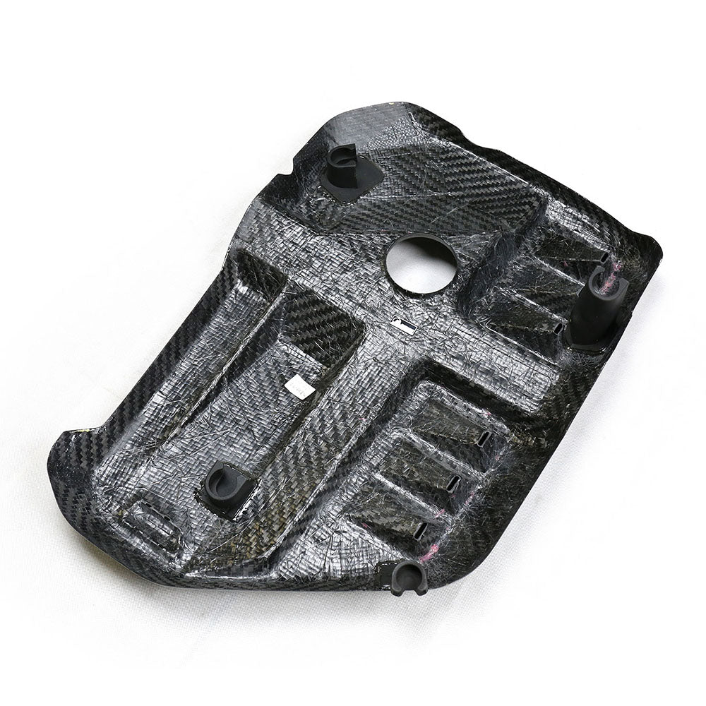 A carbon fiber automotive component with multiple molded sections and cutouts, including a central circular hole and various clips, lies on a white background.