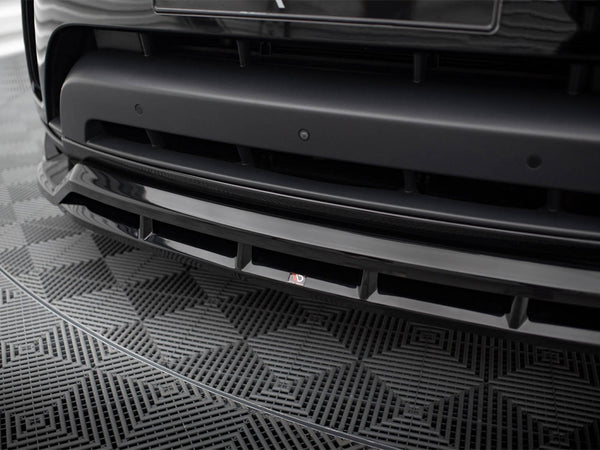 A black car's front bumper with a sleek design is shown in detail, featuring a small "3D" logo. It rests on a geometric-patterned mat.