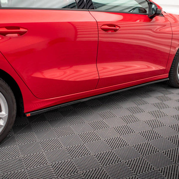 A red car with two doors and silver wheels is parked on a patterned gray floor inside a well-lit room, reflecting the structured light above.
