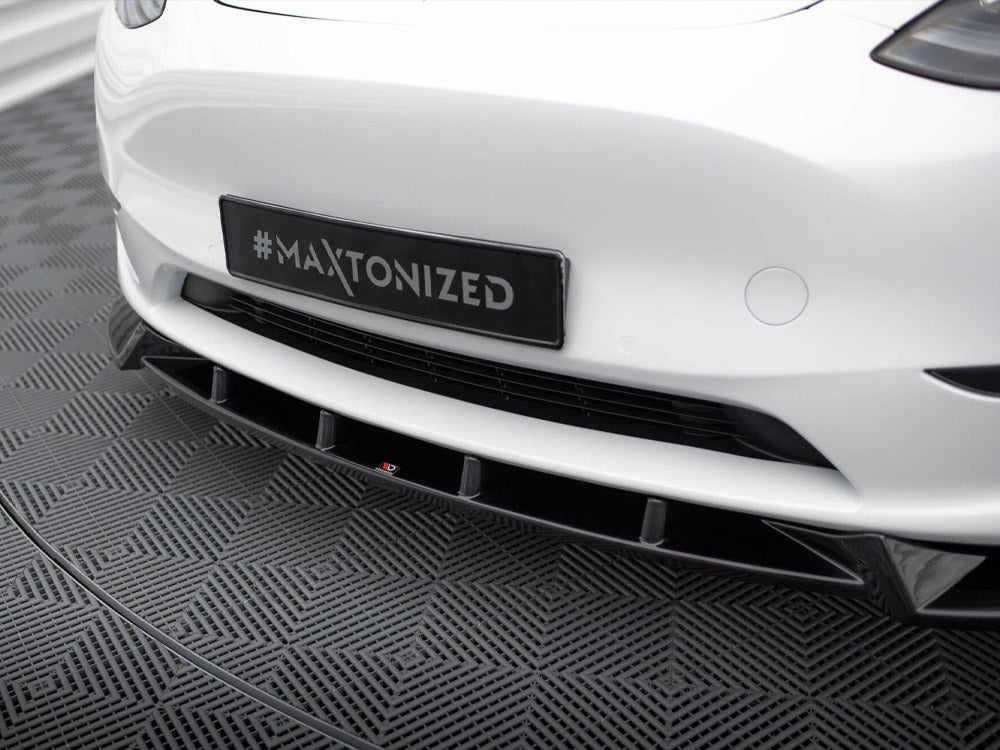 A car's front bumper, displaying a hashtag "#MAXTONIZED" on a black license plate, is shown on a textured gray patterned floor in an indoor setting.