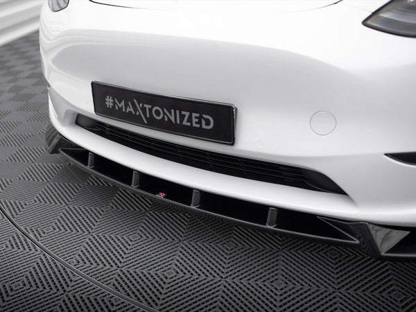 A car's front bumper, displaying a hashtag "#MAXTONIZED" on a black license plate, is shown on a textured gray patterned floor in an indoor setting.