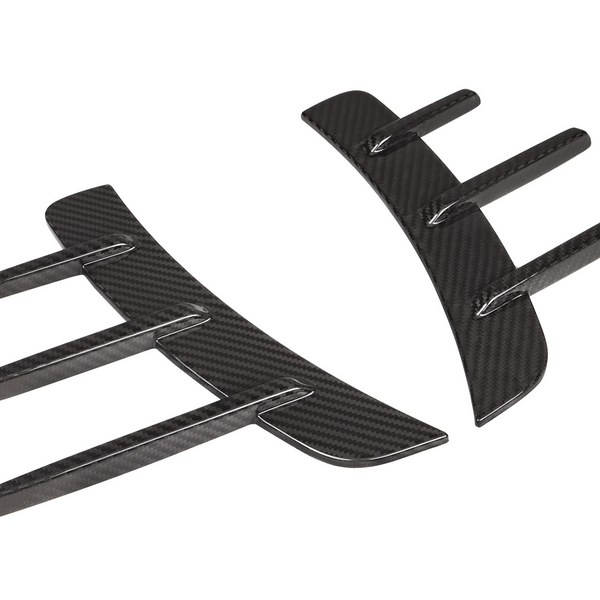 Two black carbon fiber car accessories with curved shapes and protruding fins are positioned parallel to each other on a plain white background.