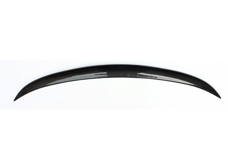 A curved carbon fiber spoiler rests against a plain white background, highlighting its glossy finish and aerodynamic design.