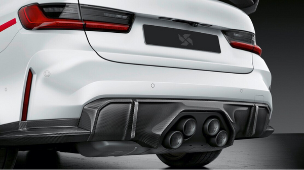 A white sports car's rear features a sleek carbon fiber diffuser with four circular exhaust tips, parked on a smooth surface in a dimly lit environment.