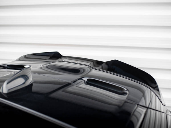 A glossy black car's hood with streamlined air vents sits stationary, reflecting light. It's positioned against a backdrop of horizontal, white, textured panels.