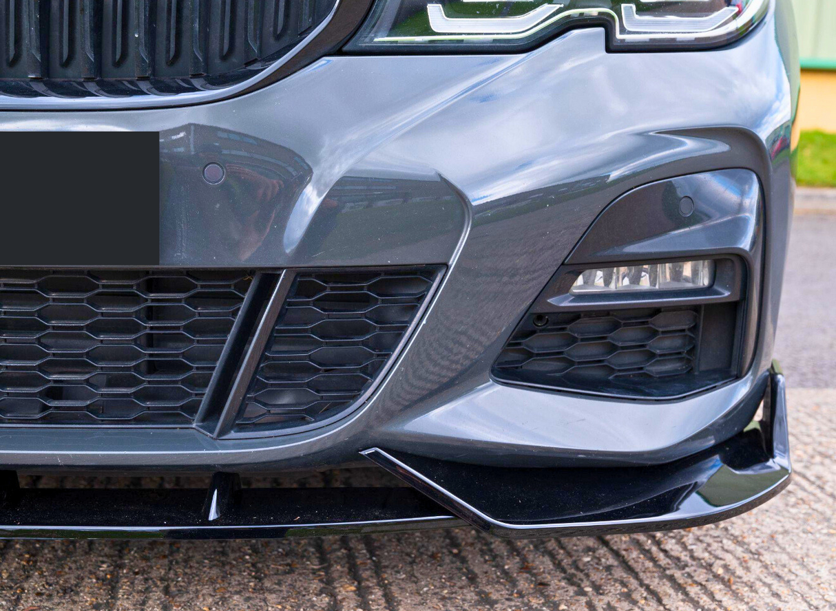 A car's front bumper with a honeycomb grille and sleek, angular design; headlight is visible in an outdoor parking area. License plate is obscured.