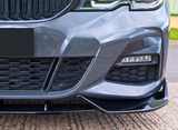A car's front bumper with a honeycomb grille and sleek, angular design; headlight is visible in an outdoor parking area. License plate is obscured.