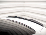 A black spoiler is positioned on a white car trunk, with a sleek design. The setting is a room with white, horizontally-lined walls, adding a modern aesthetic.