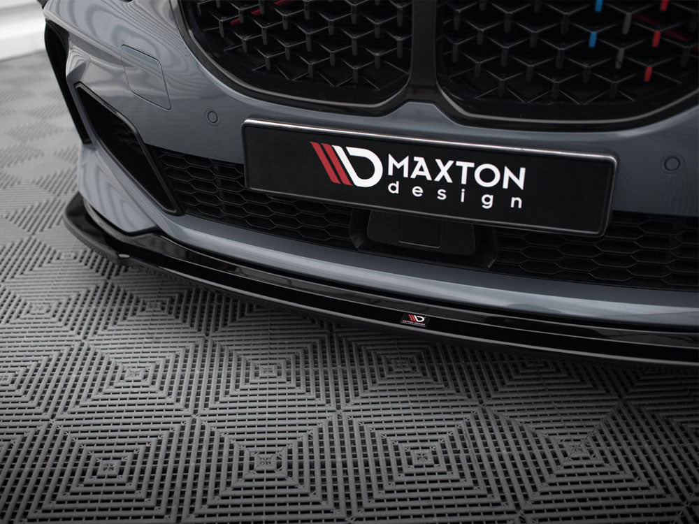 Car bumper features a "Maxton Design" logo, displayed on a patterned floor. The sleek, gray surface highlights an aesthetic grille, capturing a modern automotive design in a showroom setting.