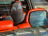 Car seats with carbon fiber backs and red accents are seen through a rear window with orange defrost lines. Sunlight reflects on the interior, highlighting the texture.