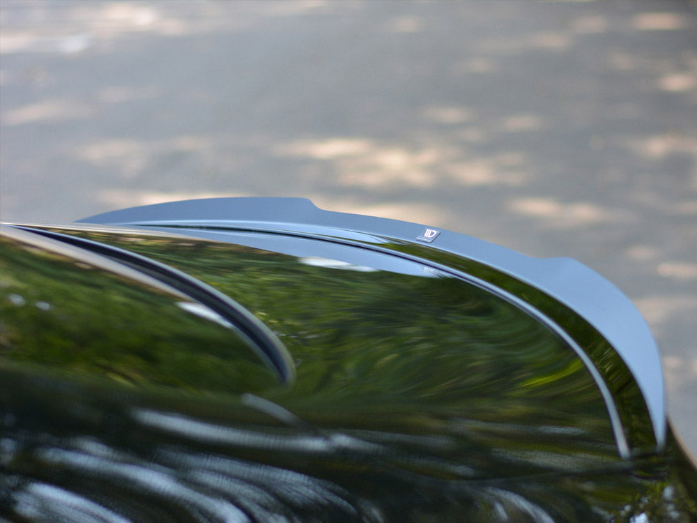 A car roof reflects blurred greenery and sky; its black surface is curved smoothly. In the background, the road appears indistinct through sunlight-dappled shadows.