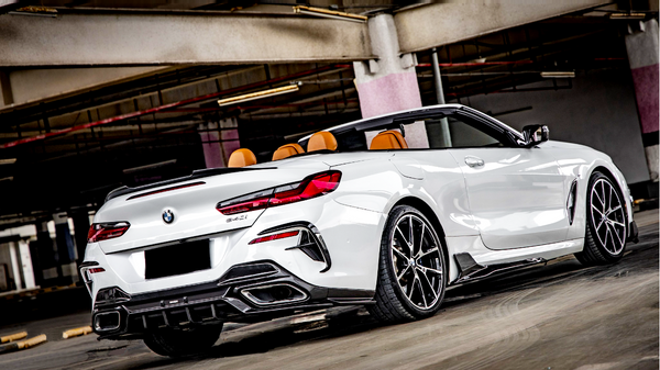 A white convertible sports car is parked in a dimly lit garage. The car features orange seats, intricate wheel designs, and visible branding on the rear, with a sleek, modern appearance.