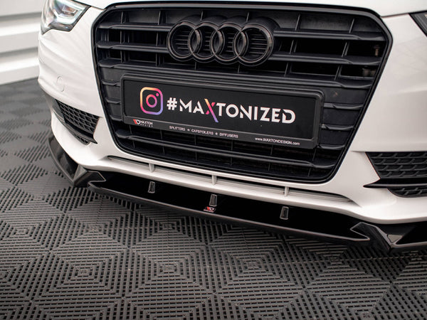 Car's front grille with Audi logo and license plate displaying text "#MAXTONIZED @MAXTONDESIGN.COM." It rests on a textured garage floor.