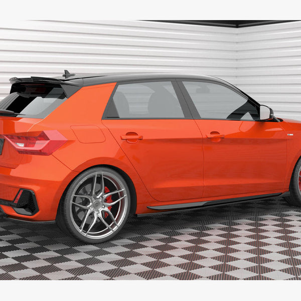 A bright orange hatchback car is parked on a checkered floor in a white-walled garage. It features silver alloy wheels and visible branding: "AUDI" and "Maxon Design".