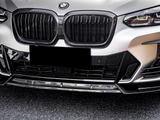 A BMW car front features a prominent grille and sleek headlights, parked on a textured asphalt surface. A black license plate obscures the lower section.