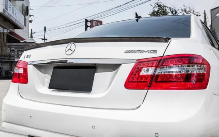 The sedan's rear, featuring Mercedes-Benz and AMG logos, displays red taillights in an urban setting with utility poles and wires.
