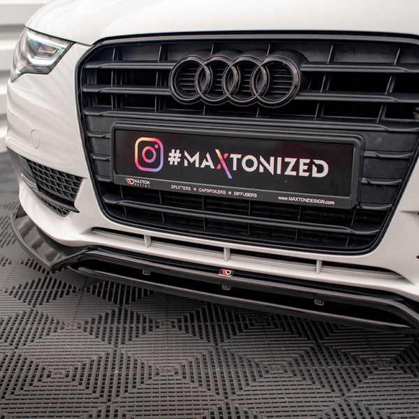 Car front bumper with Audi logo displays a license plate reading "#MAXTONIZED." The car is parked on a textured floor, surrounded by white paneling. Text: "SPLITTERS * CAPSPOILERS * DIFFUSERS * MAXTONDESIGN.COM."