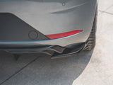 A car's rear bumper with a red reflector is parked on a sunlit, textured concrete surface, highlighting the curvature and tire tread.