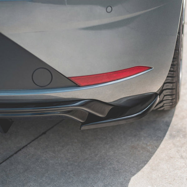 A car's rear bumper with a red reflector is parked on a sunlit, textured concrete surface, highlighting the curvature and tire tread.
