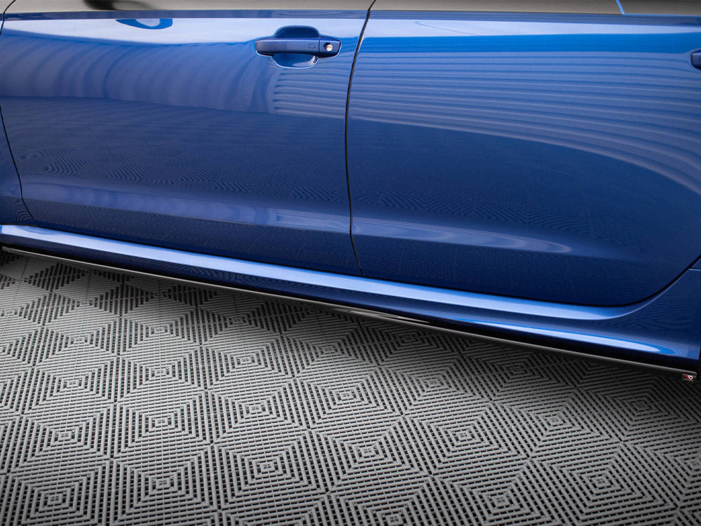 A blue car door is closed, reflecting its surroundings. Below, a gray floor features a geometric pattern, creating a contrasting backdrop in a garage or showroom setting.