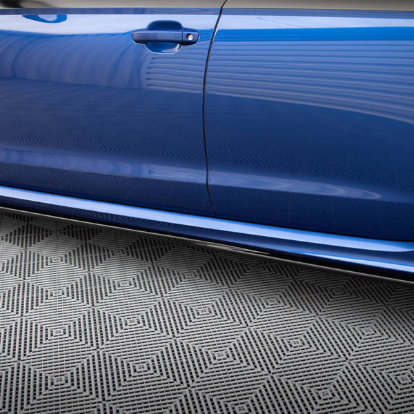 A blue car door is closed, reflecting its surroundings. Below, a gray floor features a geometric pattern, creating a contrasting backdrop in a garage or showroom setting.