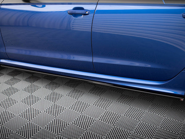 A blue car door is closed, reflecting its surroundings. Below, a gray floor features a geometric pattern, creating a contrasting backdrop in a garage or showroom setting.