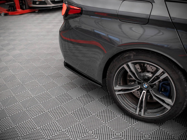 A dark gray car's rear wheel is stationary on a patterned garage floor, with a red vehicle lift partially visible in the background.