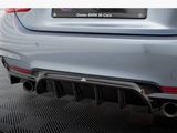 Car rear bumper with dual exhaust pipes and a black diffuser, parked on a textured surface. The license plate reads, 