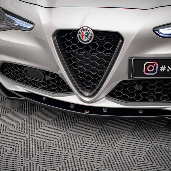 A silver car's front bumper with a hexagonal grille, prominent logo, and illuminated headlights, parked on a patterned floor. Text: "#MAXTO" and Instagram logo.
