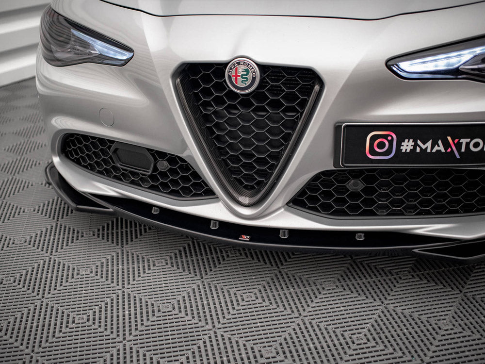A silver car's front bumper with a hexagonal grille, prominent logo, and illuminated headlights, parked on a patterned floor. Text: "#MAXTO" and Instagram logo.