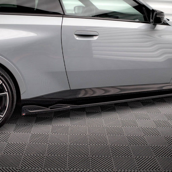 A sleek gray car with a visible wheel and side skirt detail is parked indoors on a textured floor. Brand and model emblems are visible.