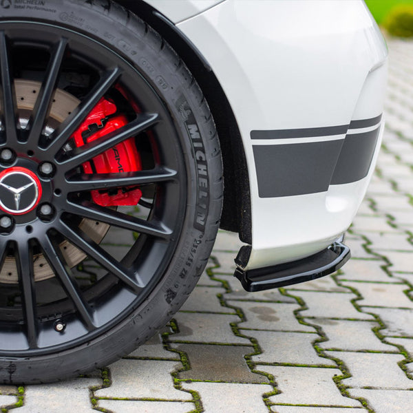 A black car wheel with a red brake caliper labeled "AMG" rests on a paved surface, adjacent to a white car body with black stripes. The tire reads "MICHELIN."