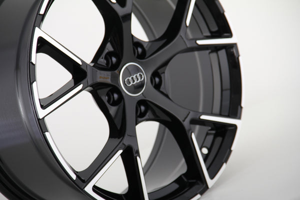 Black and silver alloy wheel, featuring a five-spoke design with the Audi logo at the center, set against a plain white background.