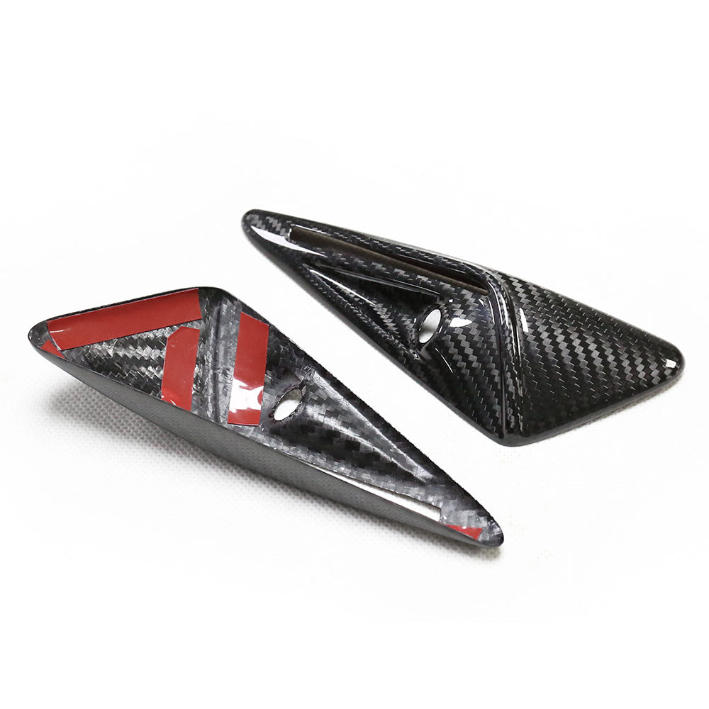 Two triangular carbon fiber pieces are positioned on a white surface. One piece has red adhesive strips and a circular hole, indicating they may be mounting components.