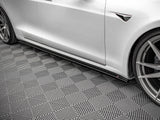 A white car with sleek, angular design rests stationary on a textured, diamond-patterned gray floor, showcasing its aerodynamic side skirts and alloy wheels in a well-lit indoor setting.