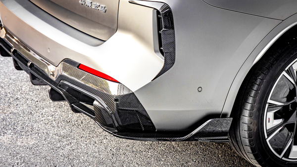 A car's rear bumper with carbon fiber details and a visible tire is parked on an asphalt surface. There is text in Chinese on the bumper.