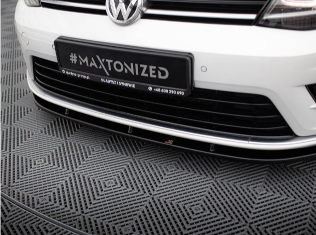A white Volkswagen car is parked on patterned flooring. The license plate displays "#MAXTONIZED." Additional text: "@dyfuzor-group.pl GLADYSZ I SYNOWIE +48 600 290 690."