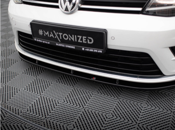 A white Volkswagen car is parked on patterned flooring. The license plate displays "#MAXTONIZED." Additional text: "@dyfuzor-group.pl GLADYSZ I SYNOWIE +48 600 290 690."