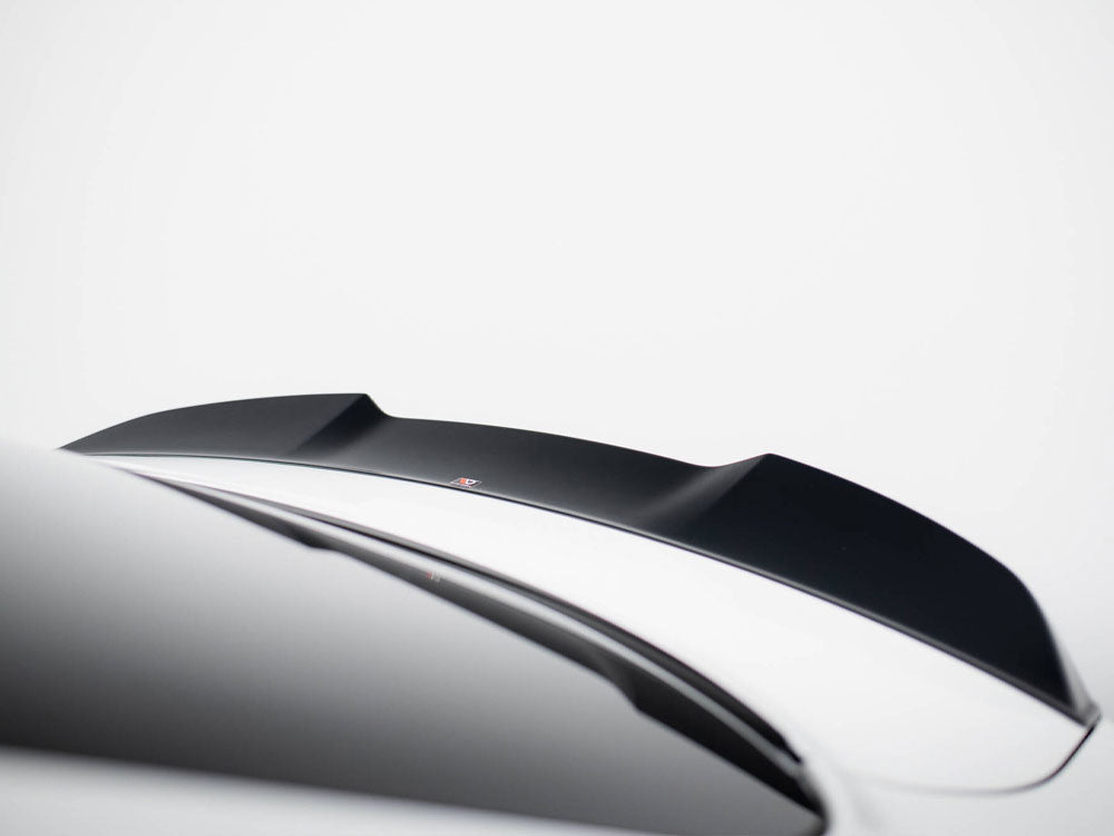 A black car spoiler is mounted on a sleek, white vehicle in a minimalistic setting. The background is a plain, light gray color, emphasizing the spoiler's contours.