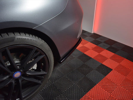 A car's rear wheel stands stationary on a checkered black and red floor in a well-lit room. The tire reads, "245/40 R 18 93 W M+S," and "OUTSIDE."