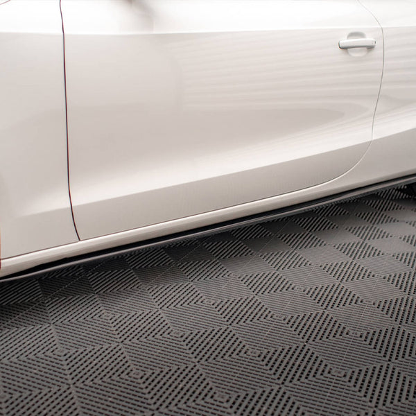 A white car with sleek design features rests on a textured garage floor, showcasing its side profile with visible wheel rims and a door handle.