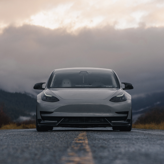 A sleek car is parked on an empty road, framed by a cloudy, mountainous landscape. The car's windshield displays the text "UNPLUGGED."