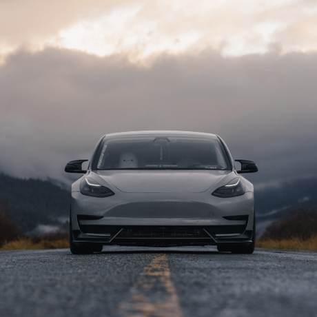 A sleek car is parked on an empty road, framed by a cloudy, mountainous landscape. The car's windshield displays the text "UNPLUGGED."