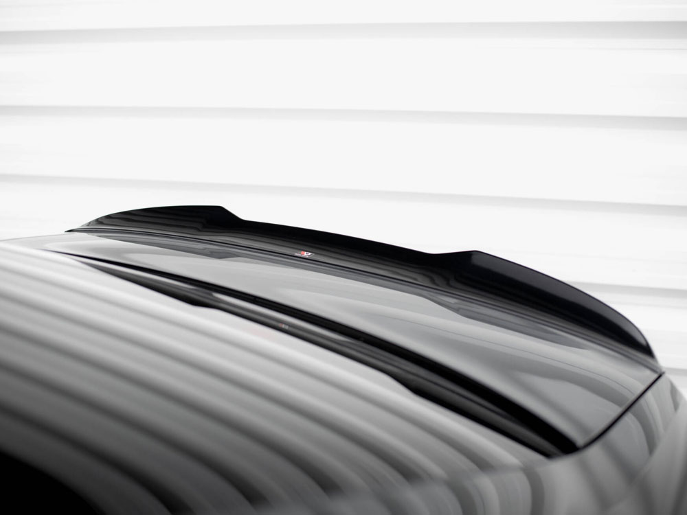 A glossy black car roof with a subtle spoiler reflects light, under a white striped ceiling, creating a sleek, modern appearance.
