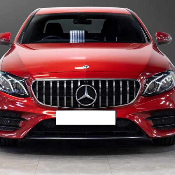 A red sedan is parked indoors, featuring a prominent grille with a silver emblem at the center, surrounded by sleek headlights. The floor is tiled and the background is plain gray.