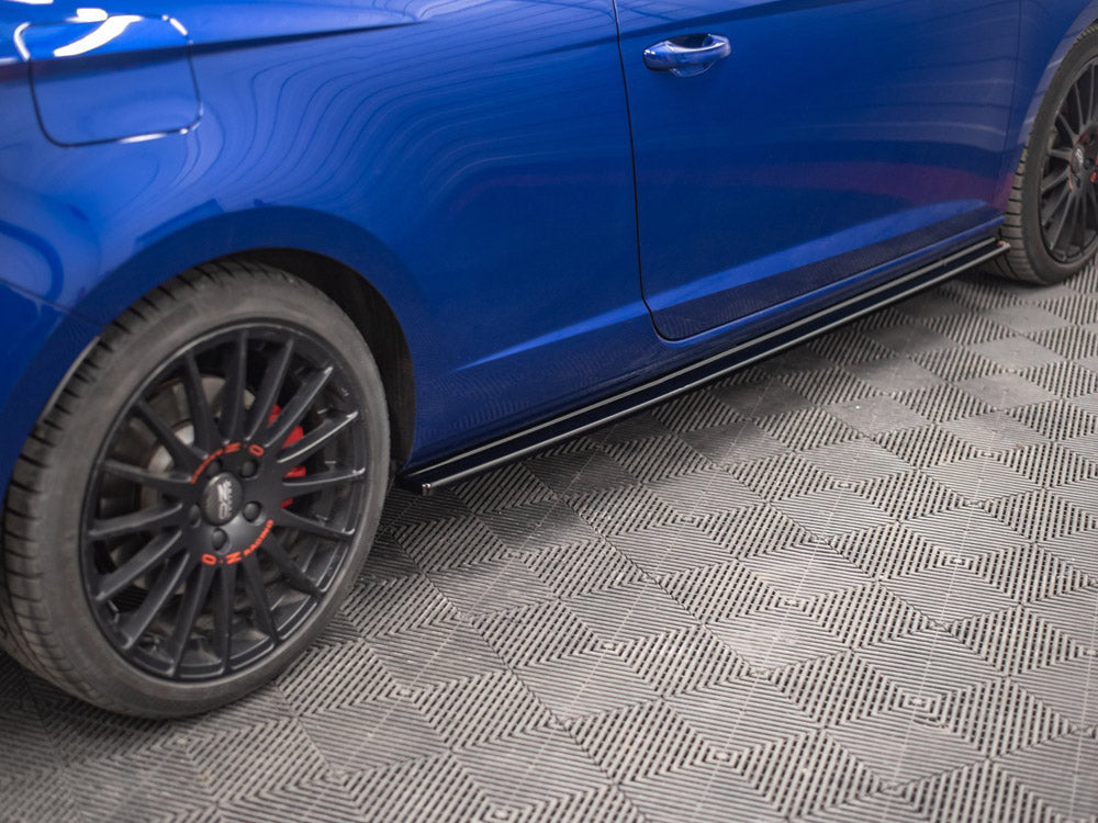 A blue car is parked on a textured gray floor. It features black wheels with red accents, and the side panel is visible with lines reflecting overhead lights.